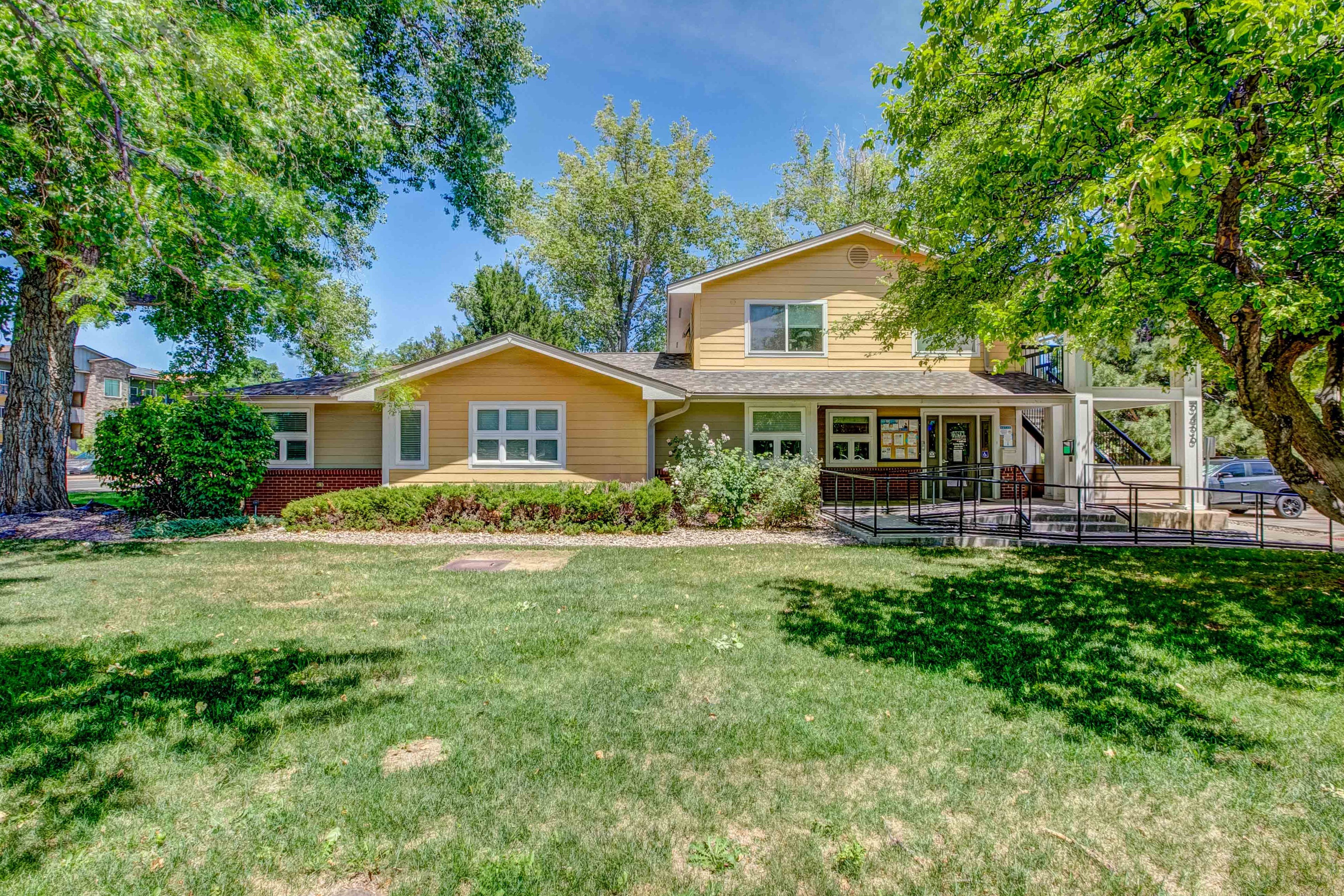 A yellow house with a white fence and trees in the background.