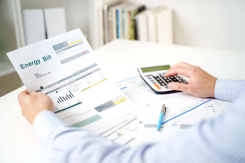 A person is reviewing an energy bill with a calculator and pen on a desk.