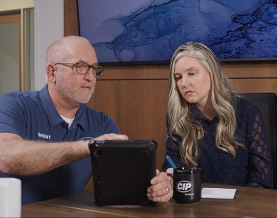A man and a woman are sitting at a table with a tablet and a mug that says CIP