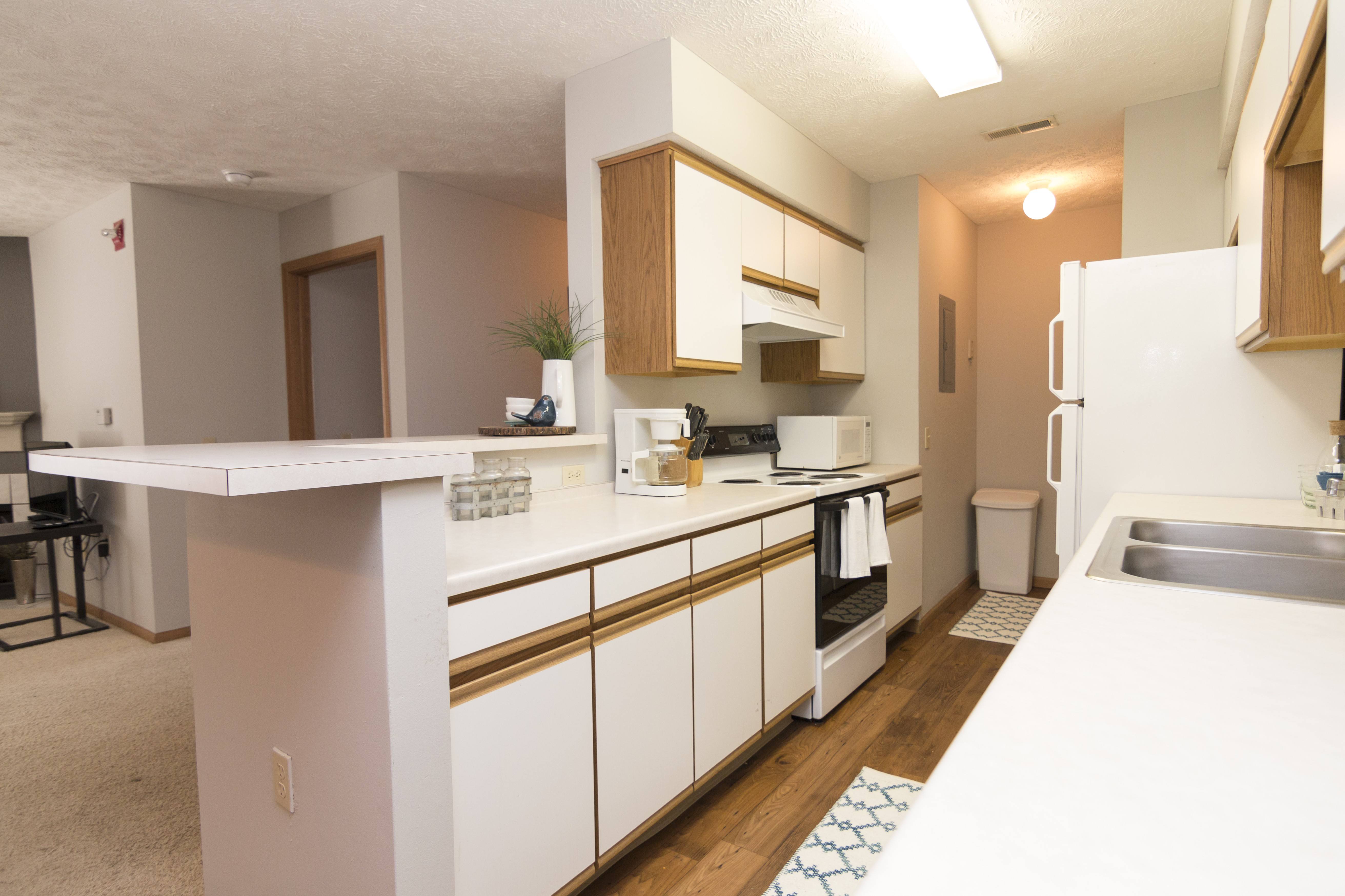 Traditional style Galley style kitchen with white cabinets and oak trim, white appliances, and warm vinyl flooring