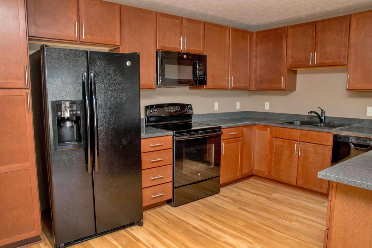 a kitchen with warm red toned brown cabinets, black appliances, and gray counters