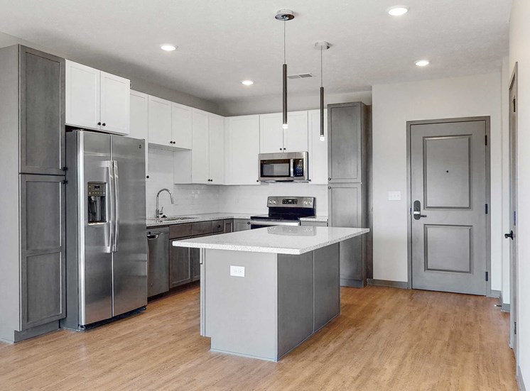Slate finish kitchen with two tone cabinets, light hard wood style flooring, granite counter tops, and white back splashes in the Bliss floor plan at Haven at Uptown in Lincoln, NE