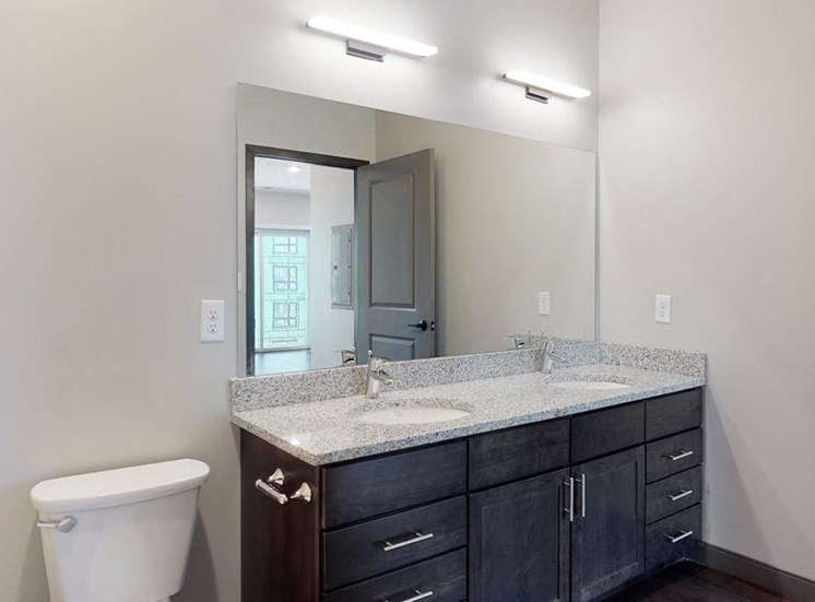 Dual sinks and light granite counter tops, as well is dark wood cabinetry for extra storage in the bathroom at Haven at Uptown in Linooln, NE