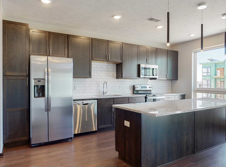 Spacious kitchen completed in the dual tone slate finish, including dark wood cabinets, dark wood style flooring, light granite counter tops, and white tile back splash in the Melody floor plan at Haven at Uptown in Lincoln, NE