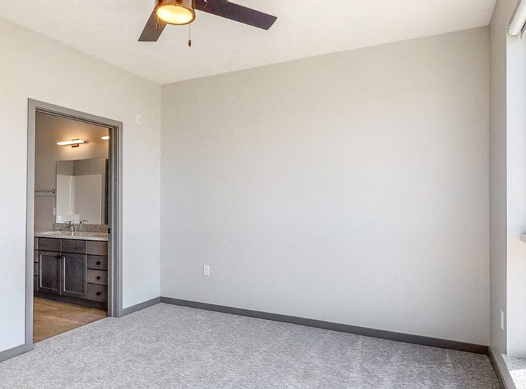 Master bedroom with large windows providing natural light, ceiling fan, and attached bathroom at Haven at Uptown in Lincoln, NE