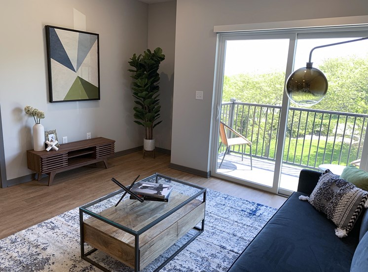 Spacious furnished living room with hard wood style flooring and scenic view of tree line in Lincoln at Haven at Uptown.