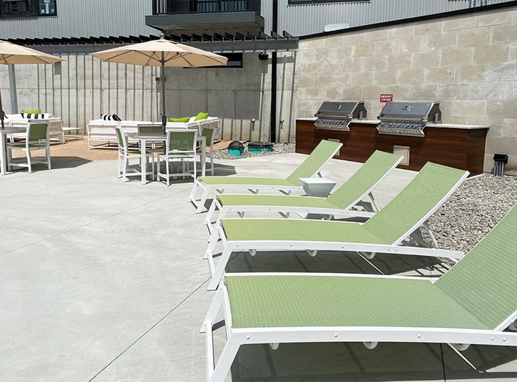 Row of light green lounge chairs and table with umbrellas near the pool at Haven at Uptown.