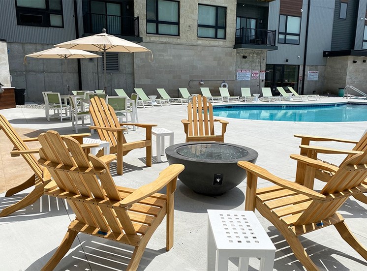 Wood Adirondack chairs arranged around a firepit near an outdoor pool at Haven at Uptown.