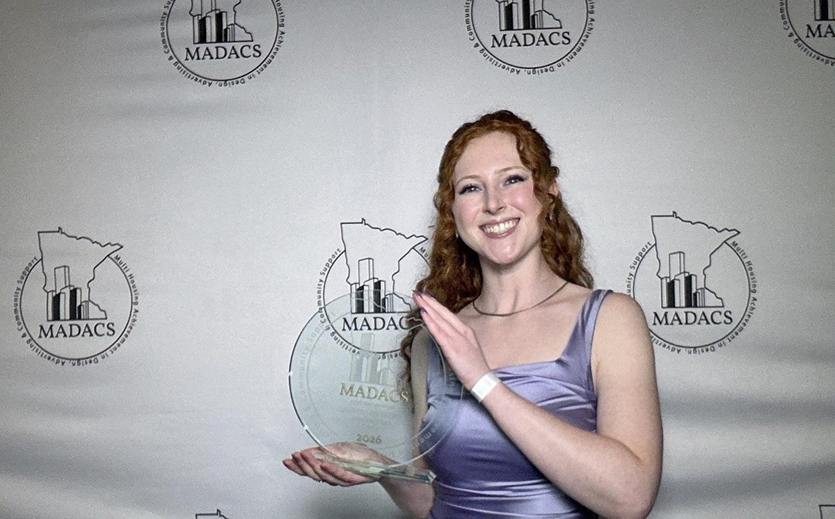 Smiling award recipient holds a glass MADACS 2026 trophy in front of a branded MADACS event backdrop