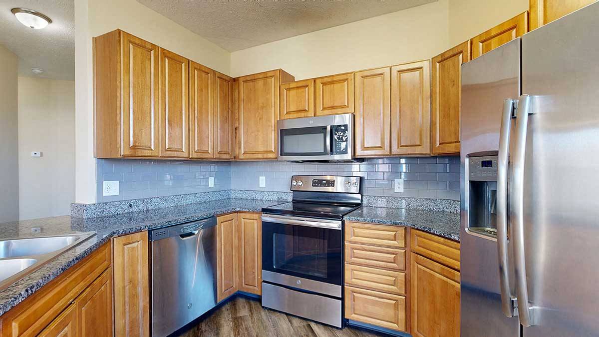 Renovated style a kitchen with granite countertops, wooden cabinets, a tile backsplash, and stainless steel appliances