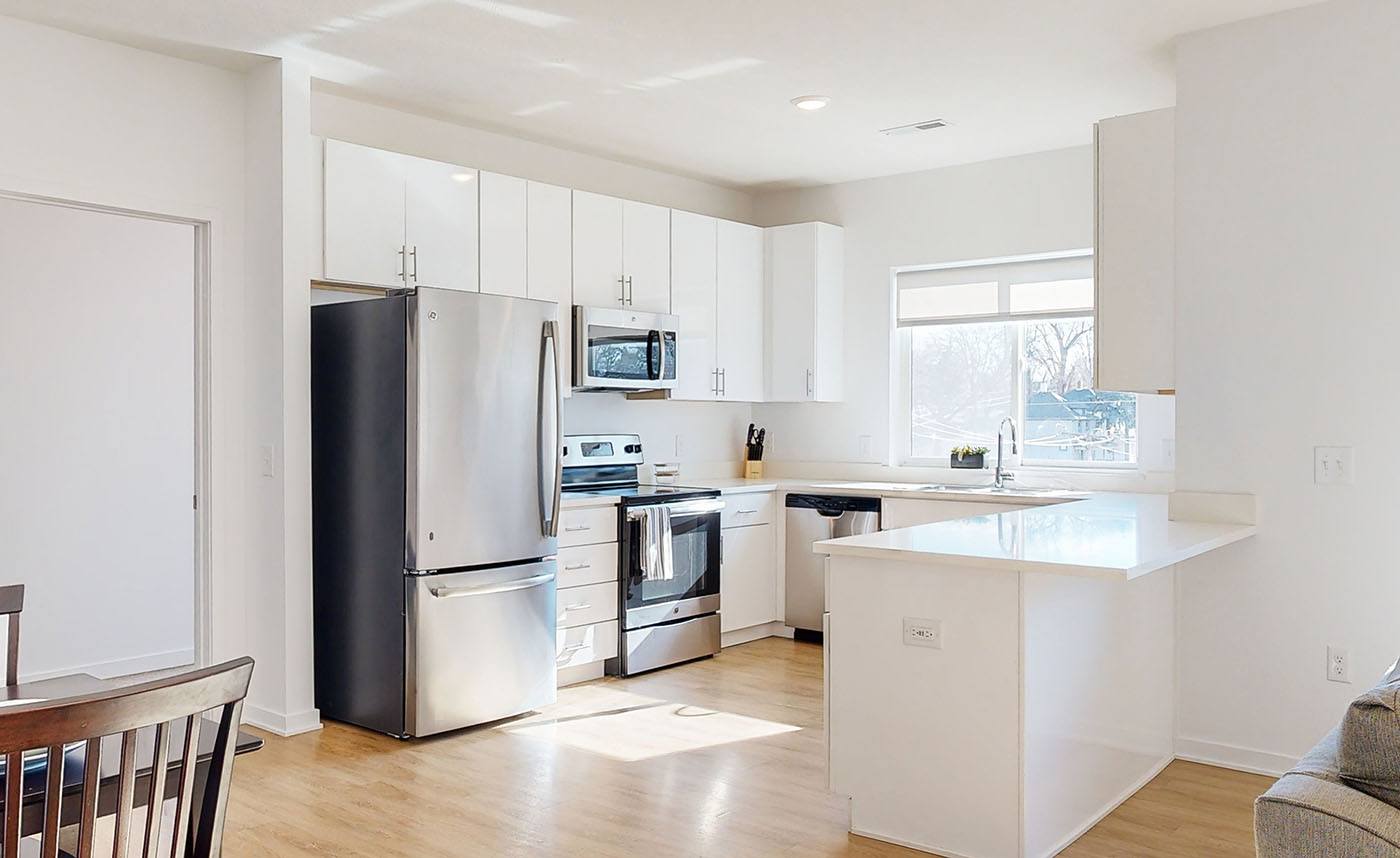 A modern apartment kitchen with white cabinets and stainless steel appliances.