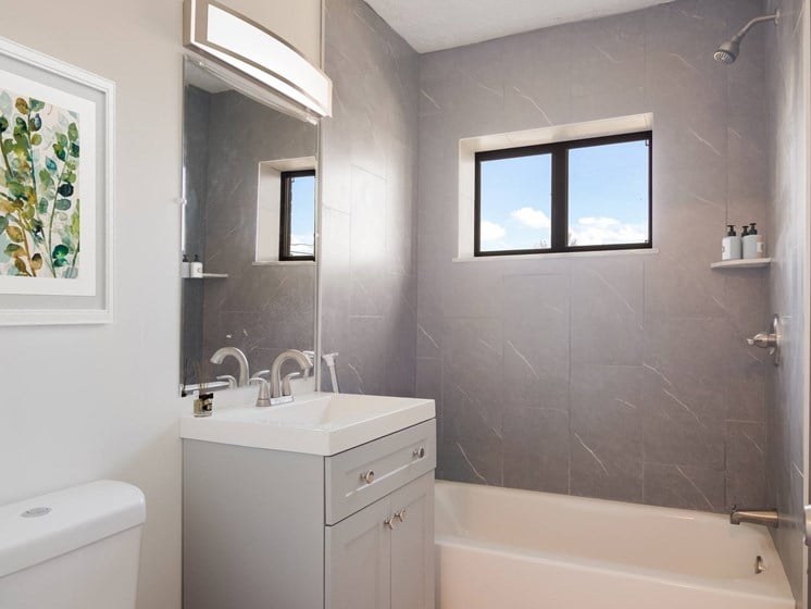 a bathroom with grey tiles and a white sink and bathtub