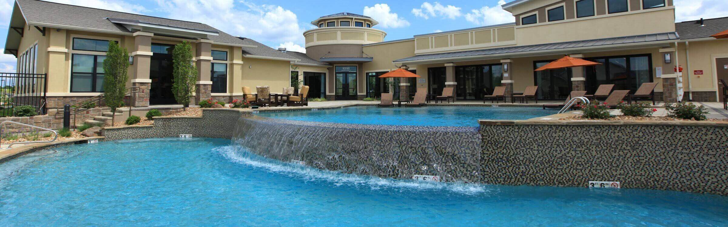 a large pool with a waterfall in front of a house  at Prairie Creek Apartments & Townhomes, Kansas