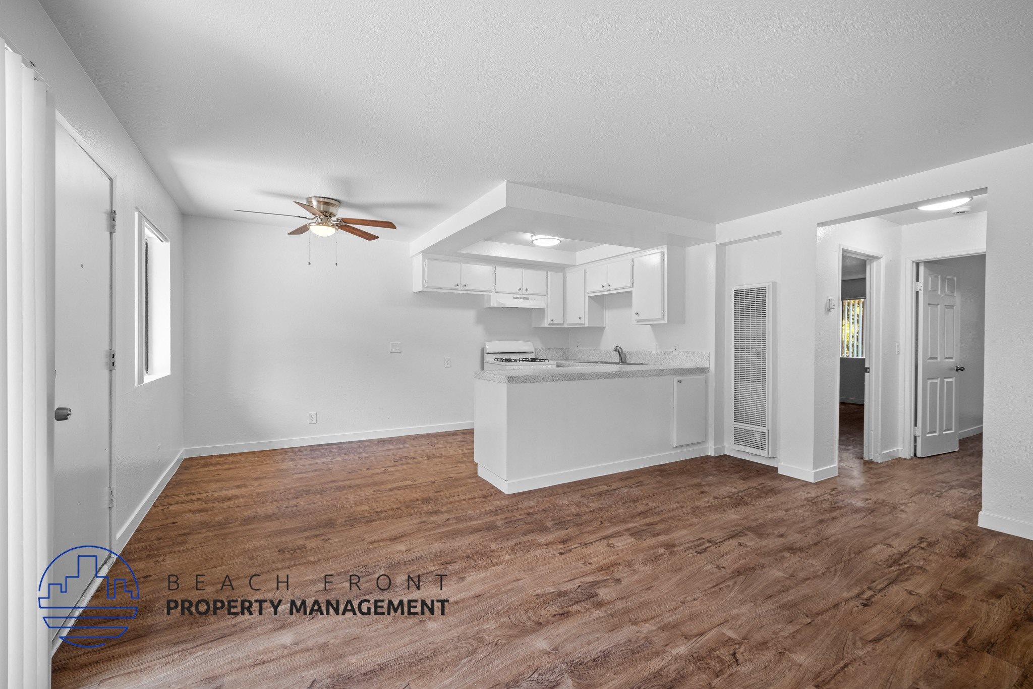 the living room and kitchen of a house with white walls and a wooden floor,the living room and kitchen of a house with white walls and a wooden floor