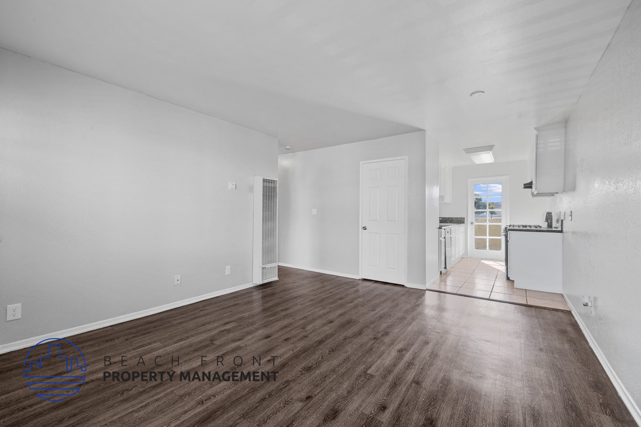 A spacious room with wooden flooring and white walls, with a logo for Beach Front Property Management in the bottom left corner.