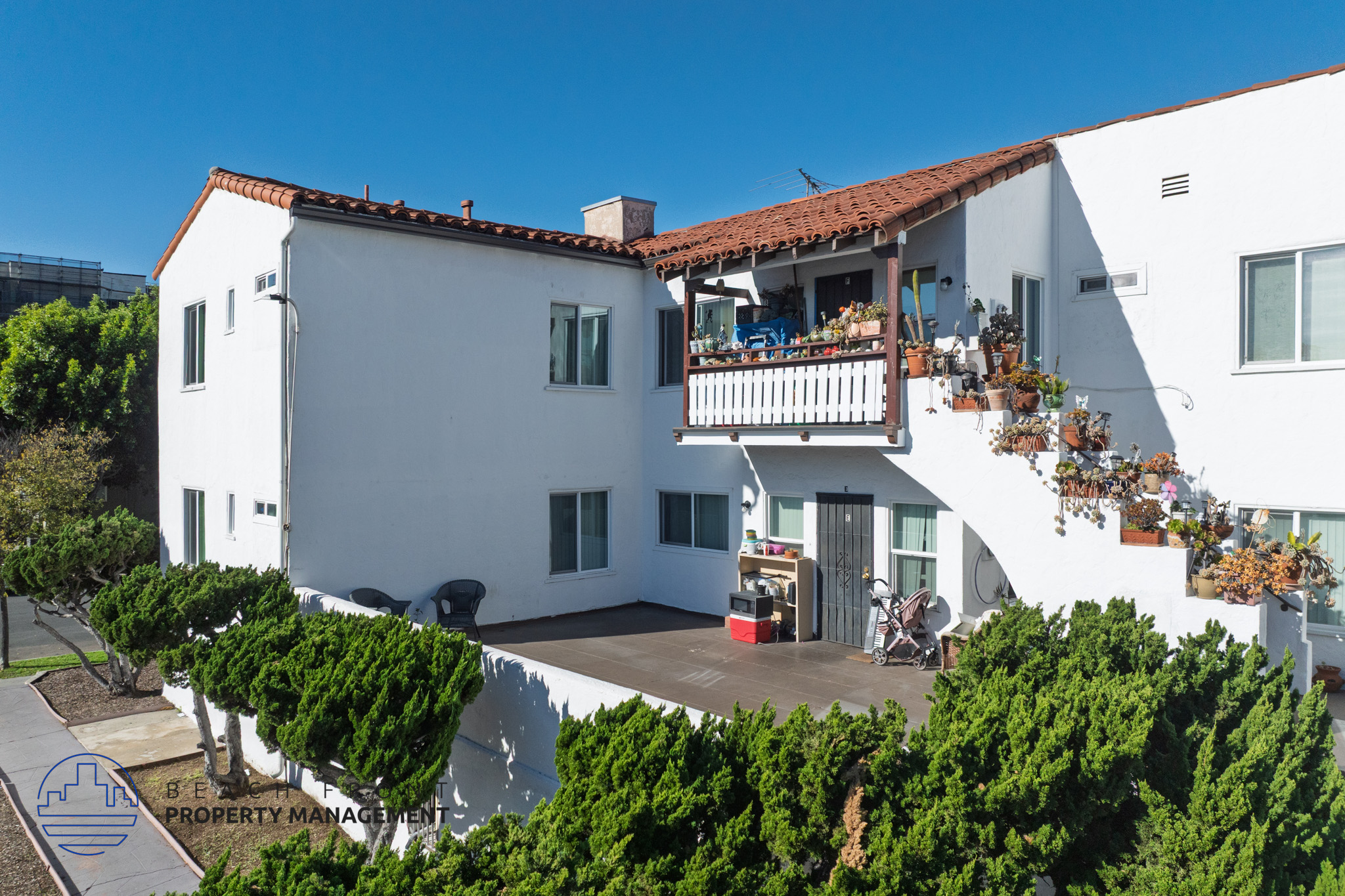 A white house with a red tile roof and a balcony with chairs and plants.