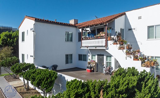 A white house with a red tile roof and a balcony with chairs and plants.