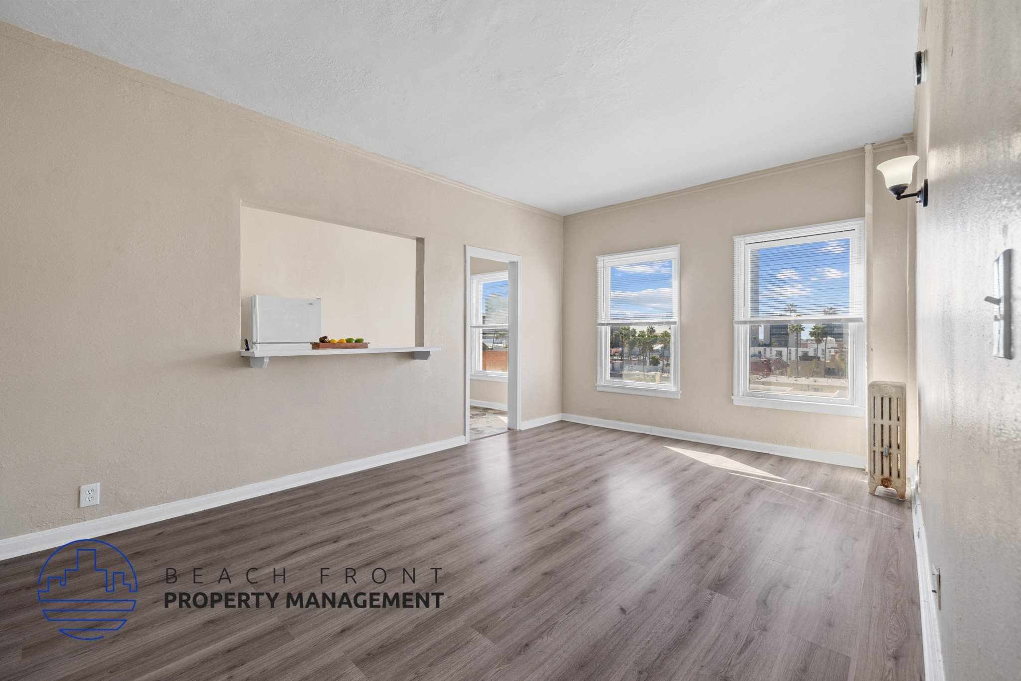 A spacious room with wooden flooring and a view of K-town through the windows.