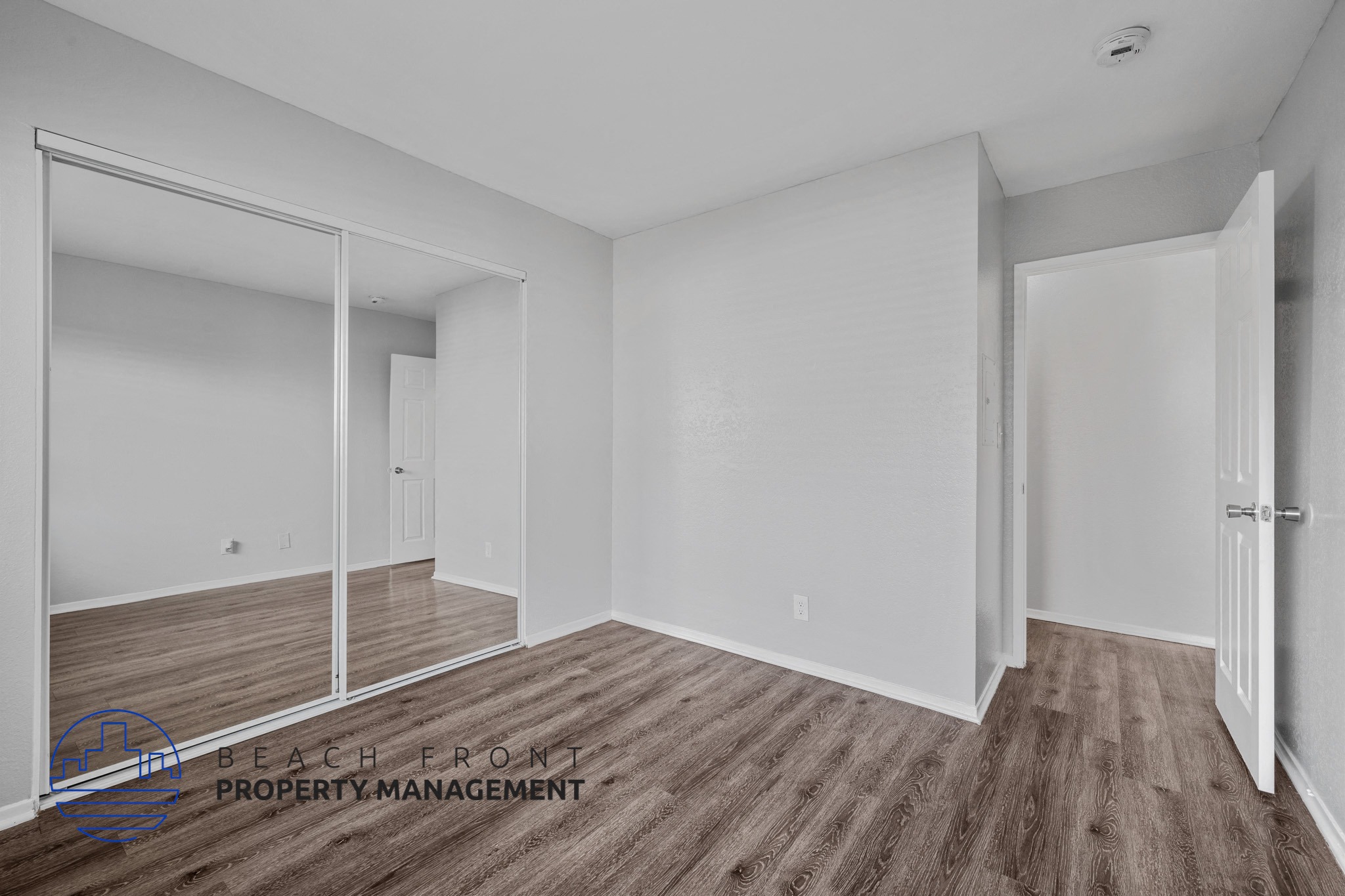 A room with wooden flooring and white walls, with a mirror on the left side.