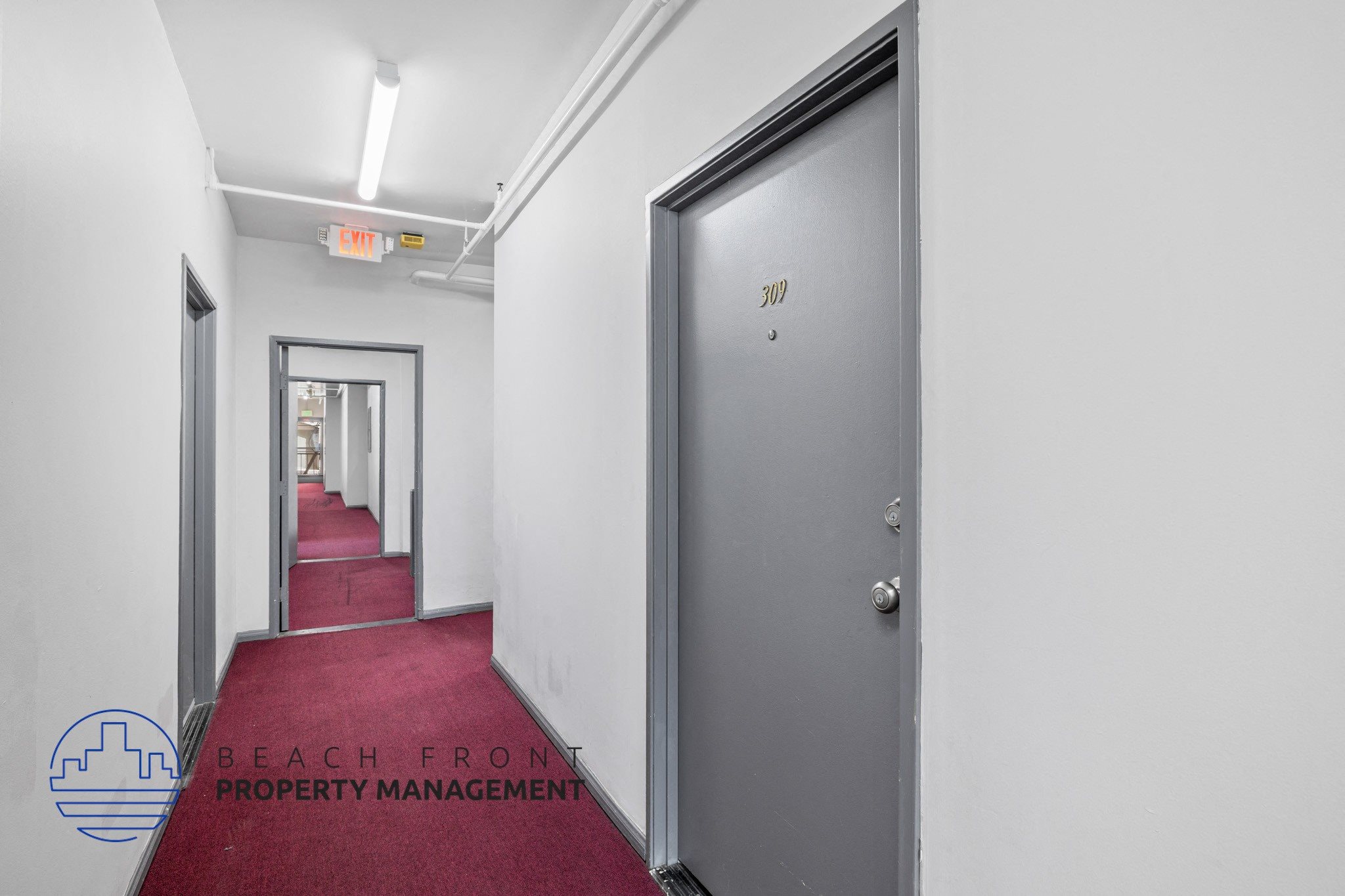 A hallway with a red carpet and a door on the right.