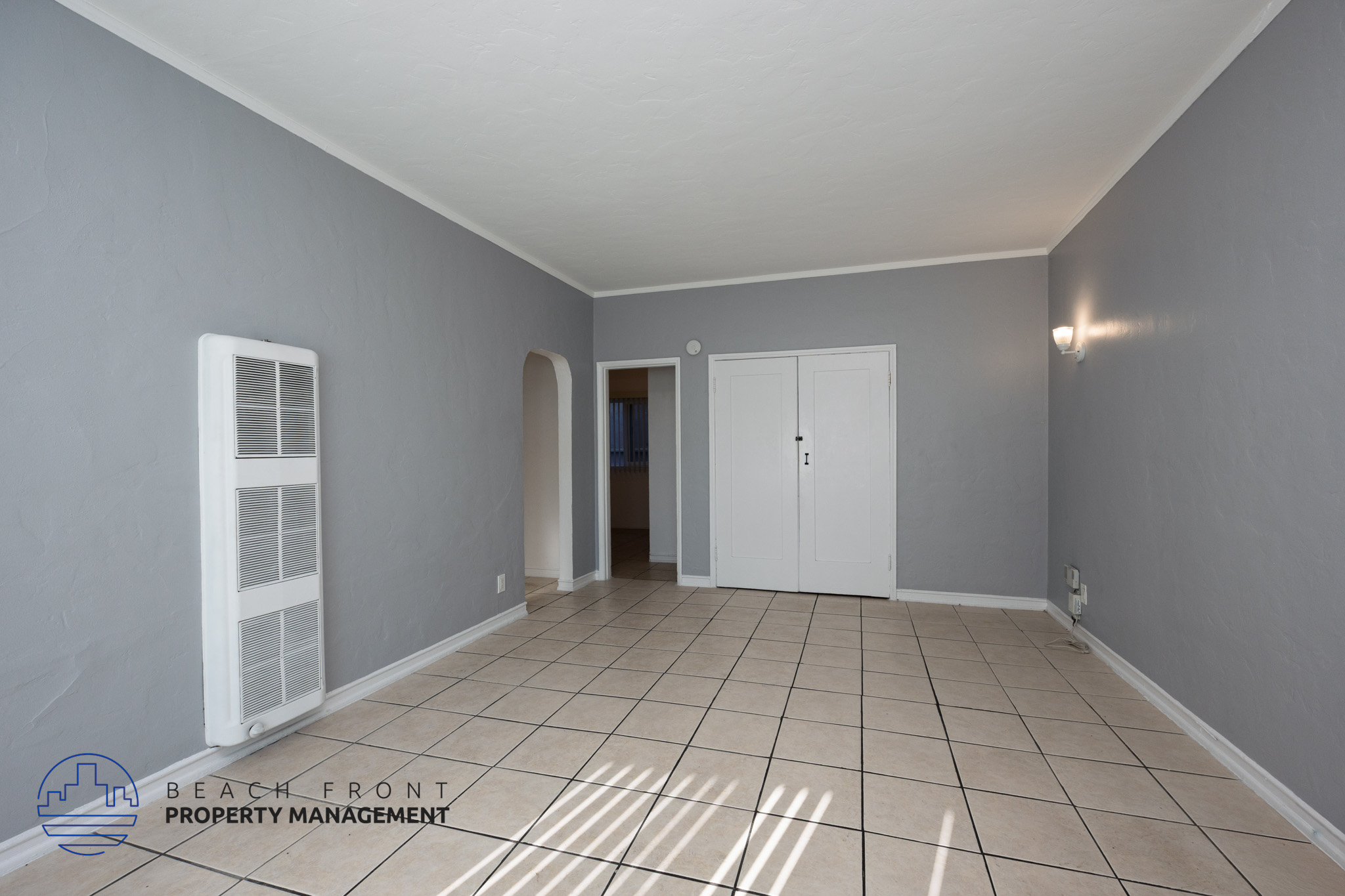 A spacious room with tiled flooring and white doors and windows.