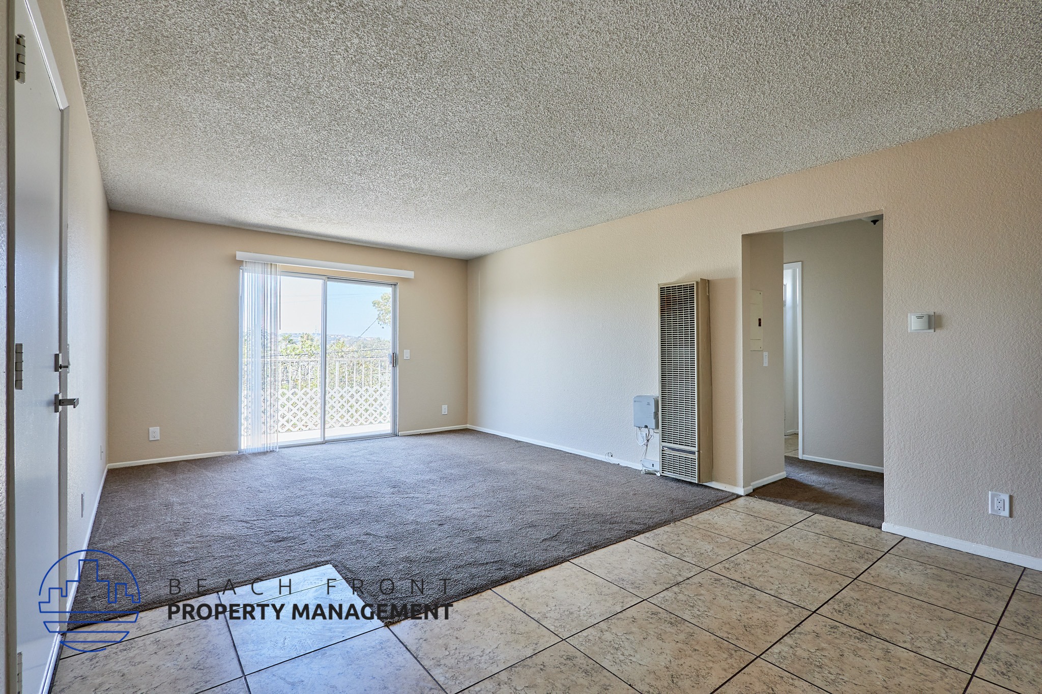 A spacious room with a carpeted floor and a sliding glass door leading to a balcony.