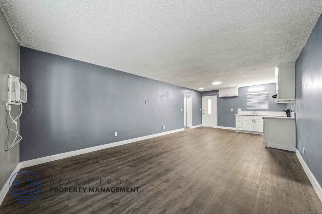 A spacious room with wooden flooring and a kitchenette in the background.
