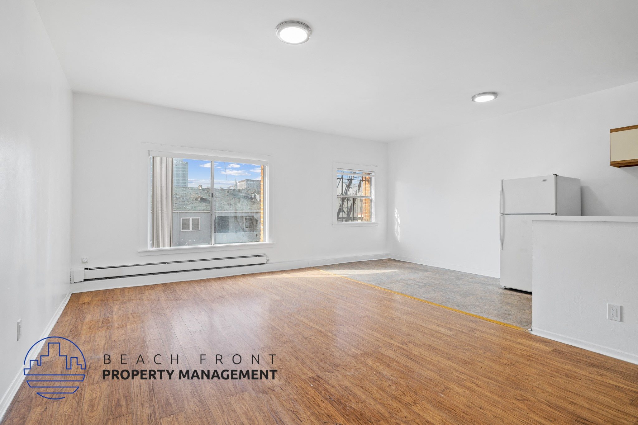 A spacious room with wooden flooring and a large window overlooking a beachfront.