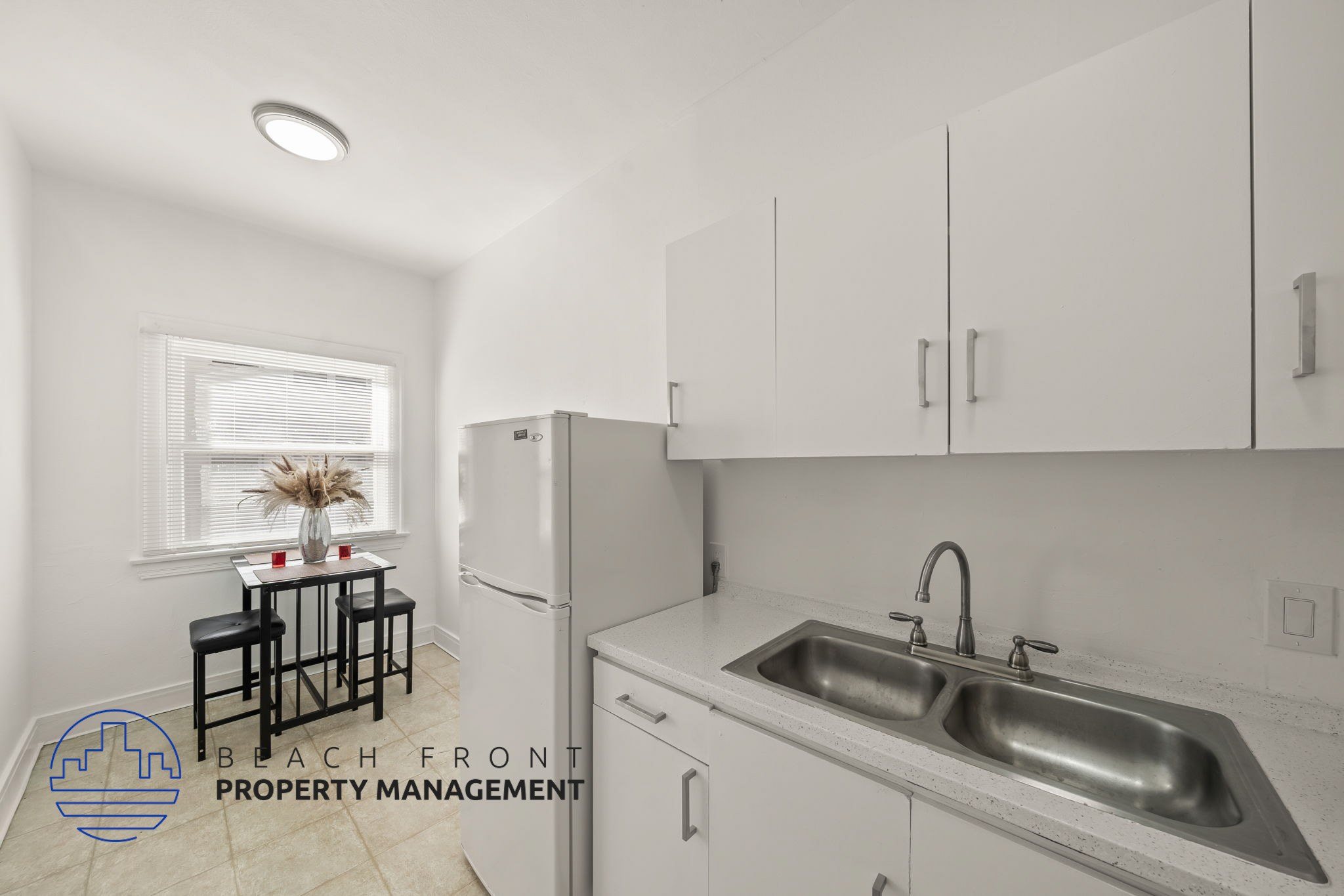 A kitchen with a sink, refrigerator, and a window with a table and chairs.