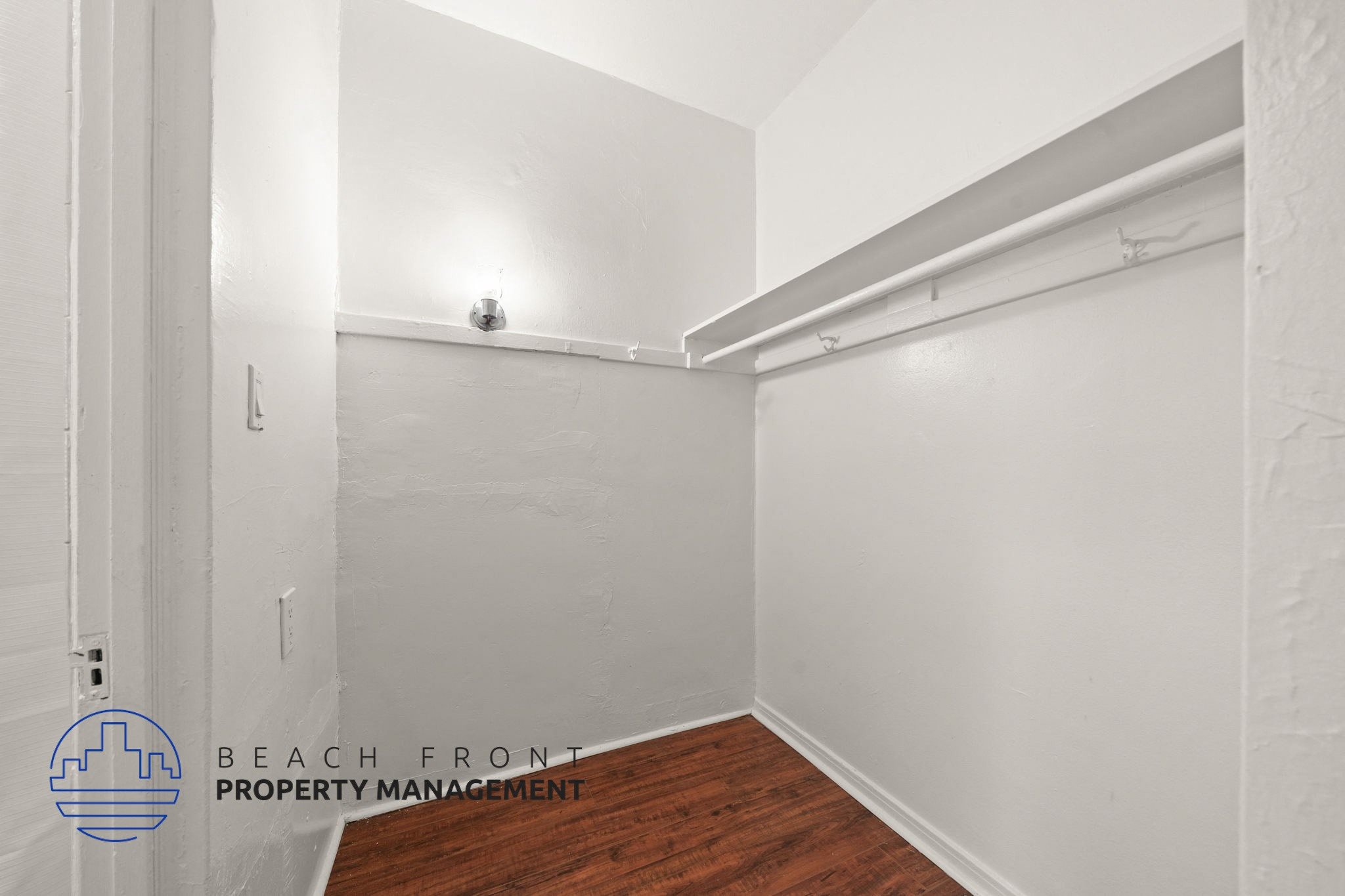 A white room with a wooden floor and a white wall with a pipe running along it.