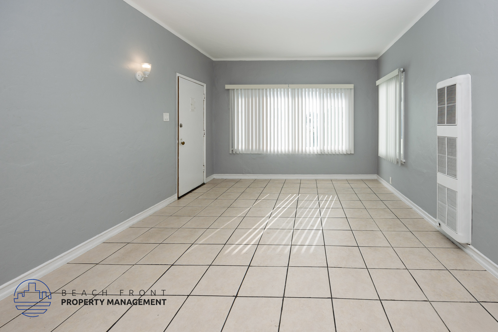 A spacious room with tiled flooring and a window with blinds.