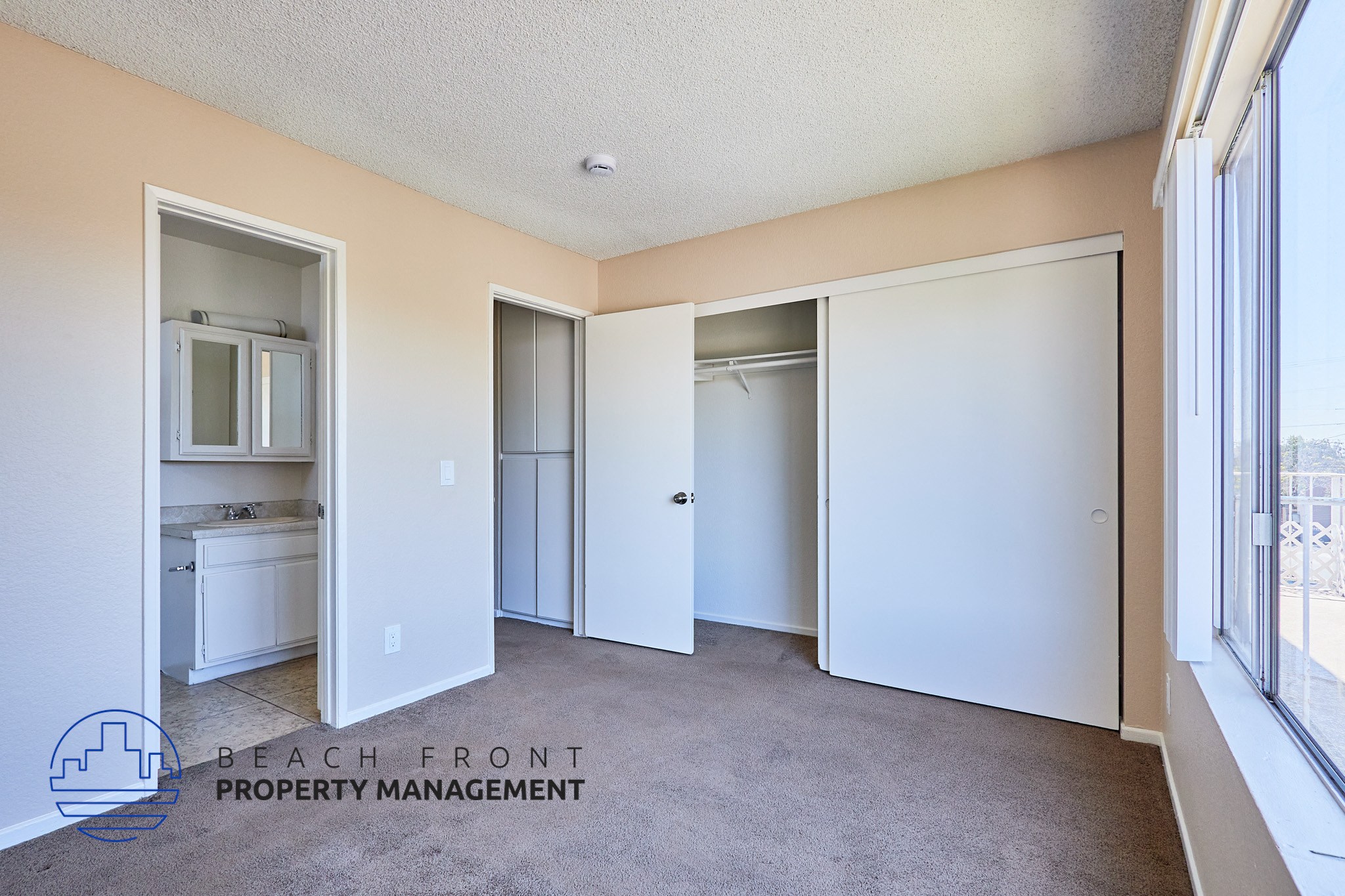 A spacious room with a carpeted floor and a large window on the right side.