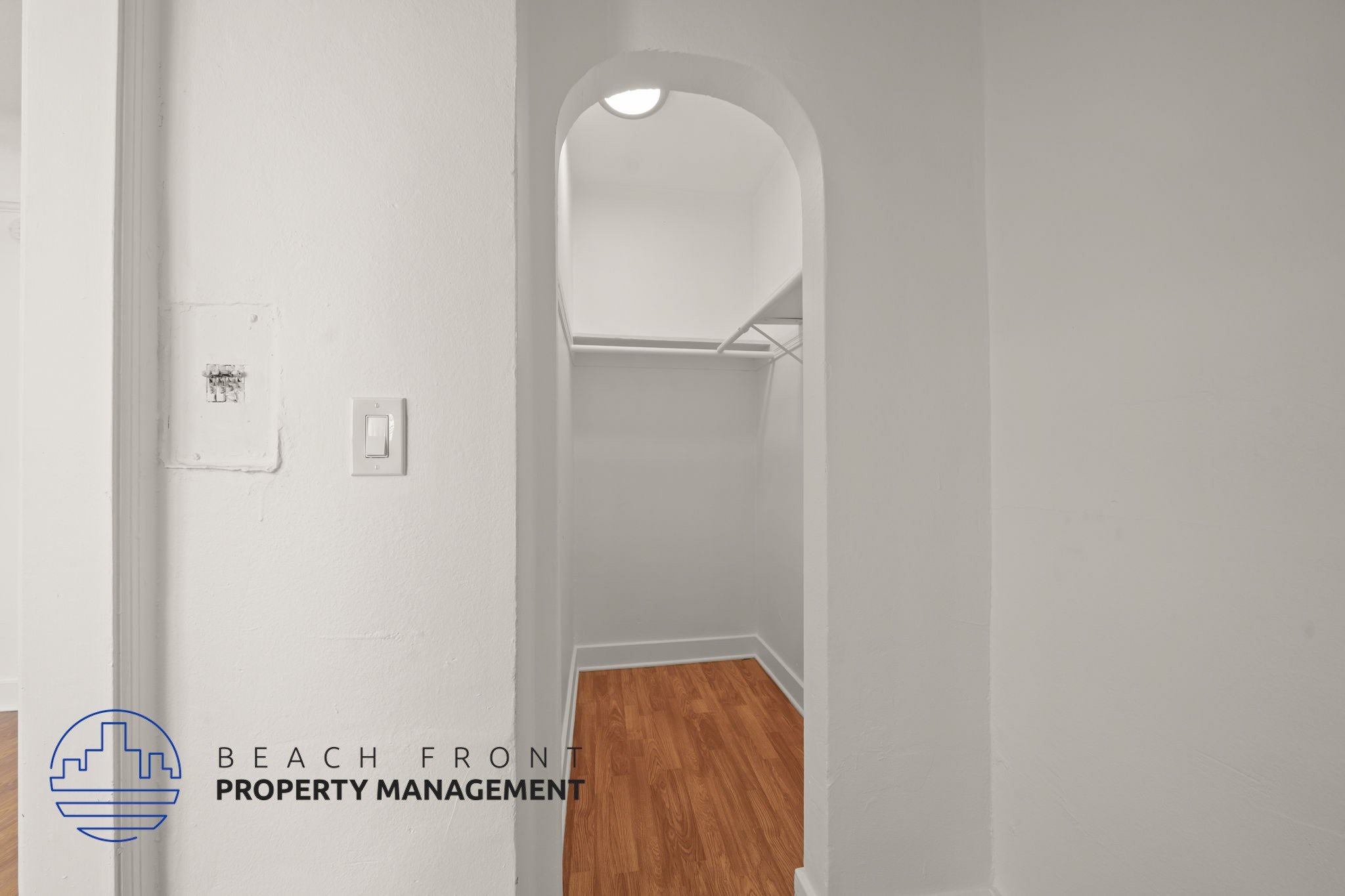 A white hallway with a wooden floor and a logo for Beach Front Property Management.