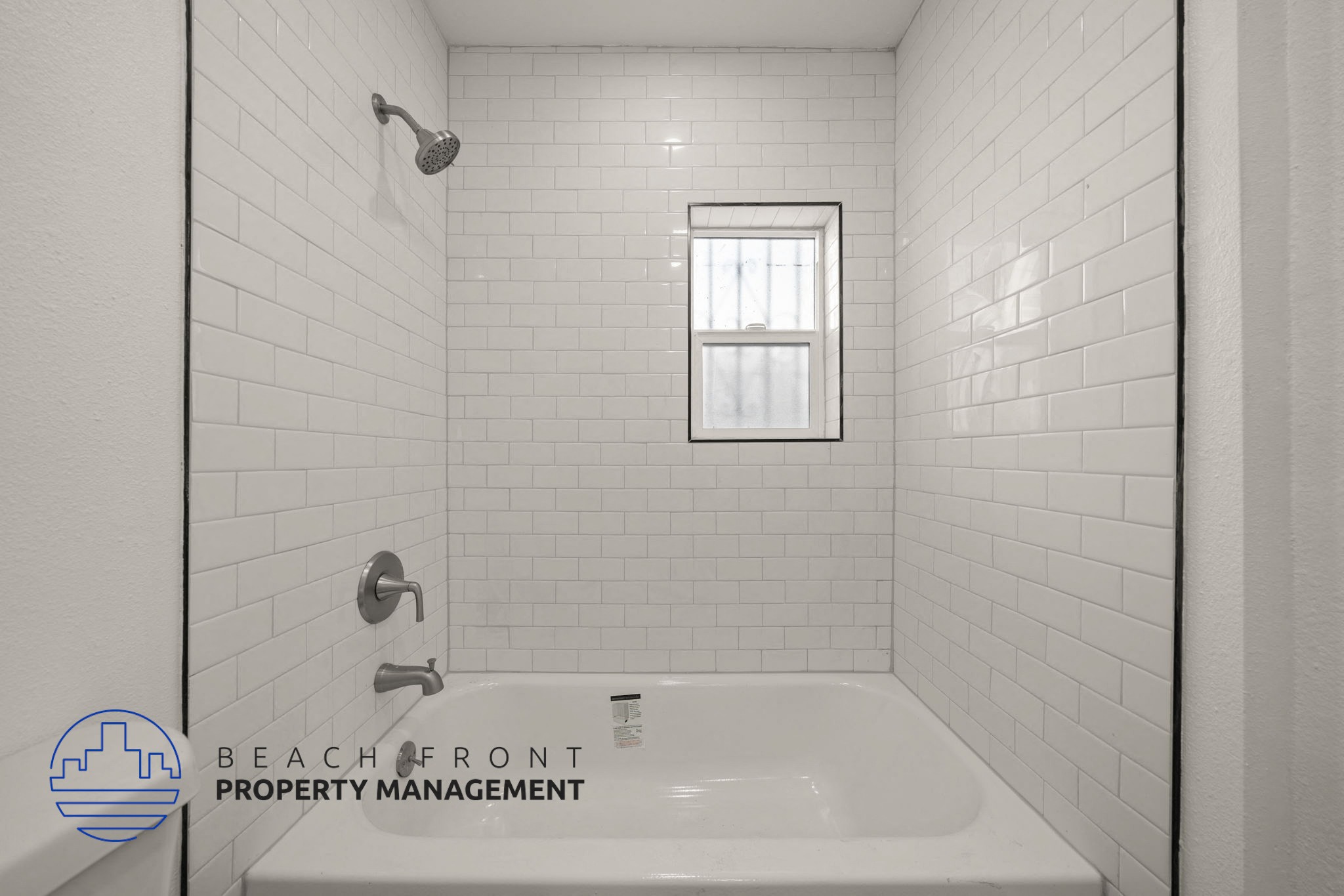 A white tiled bathroom with a shower, sink, and window.