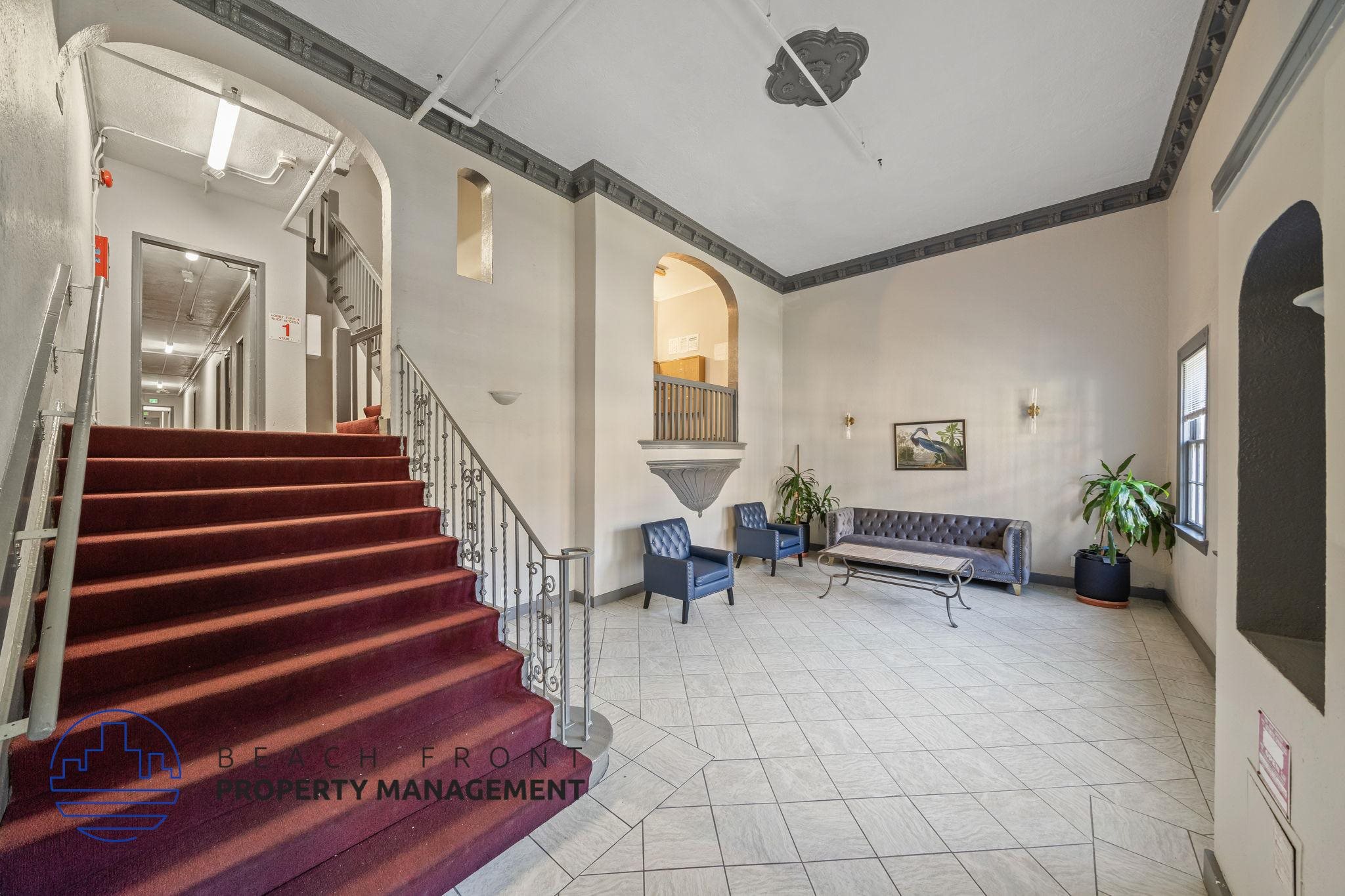 A staircase with a metal railing leads to a landing with a couch and two chairs.