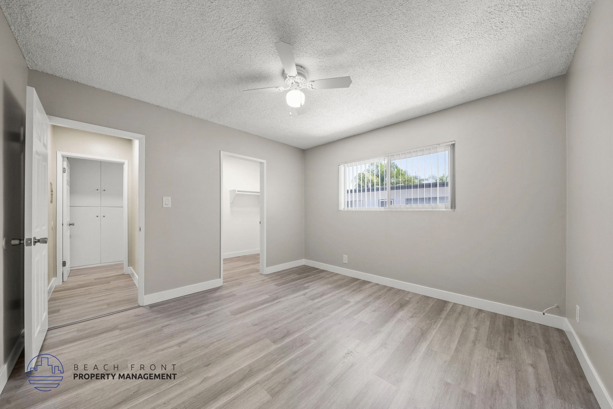 A spacious room with wooden flooring and a window overlooking a parking lot.