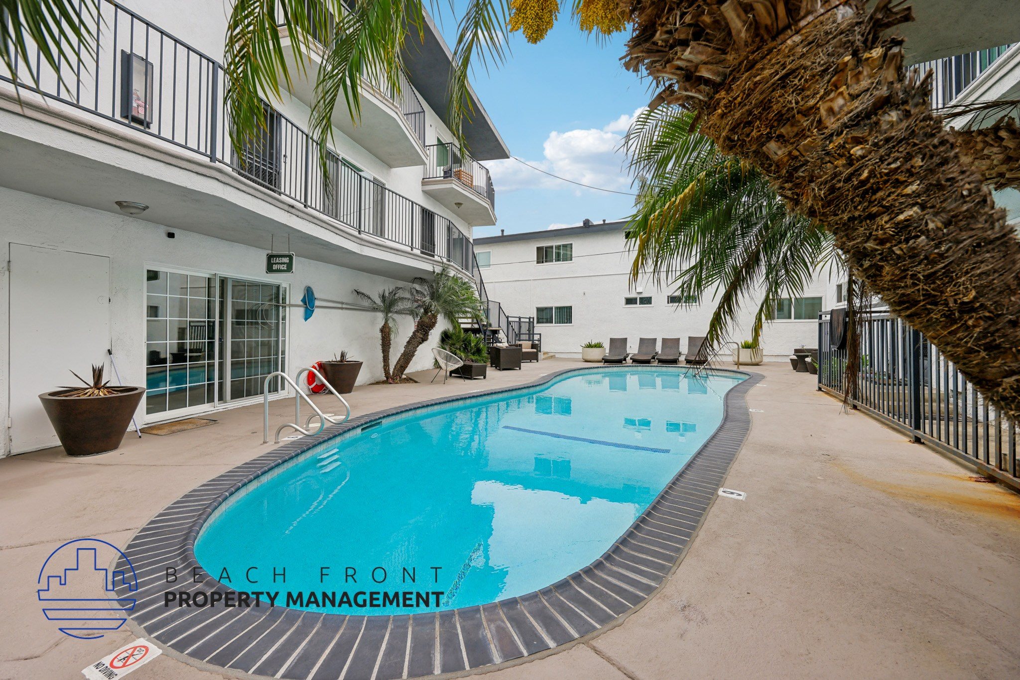 A pool surrounded by a fence and a building with a balcony.