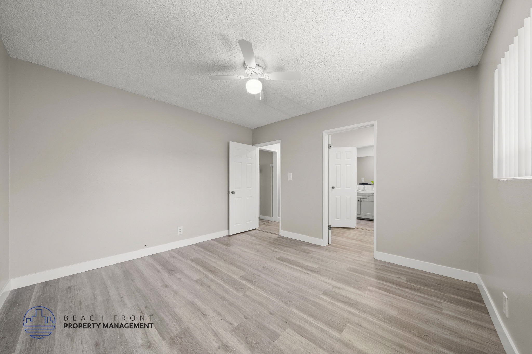 A spacious room with a ceiling fan and light, and a wooden floor.