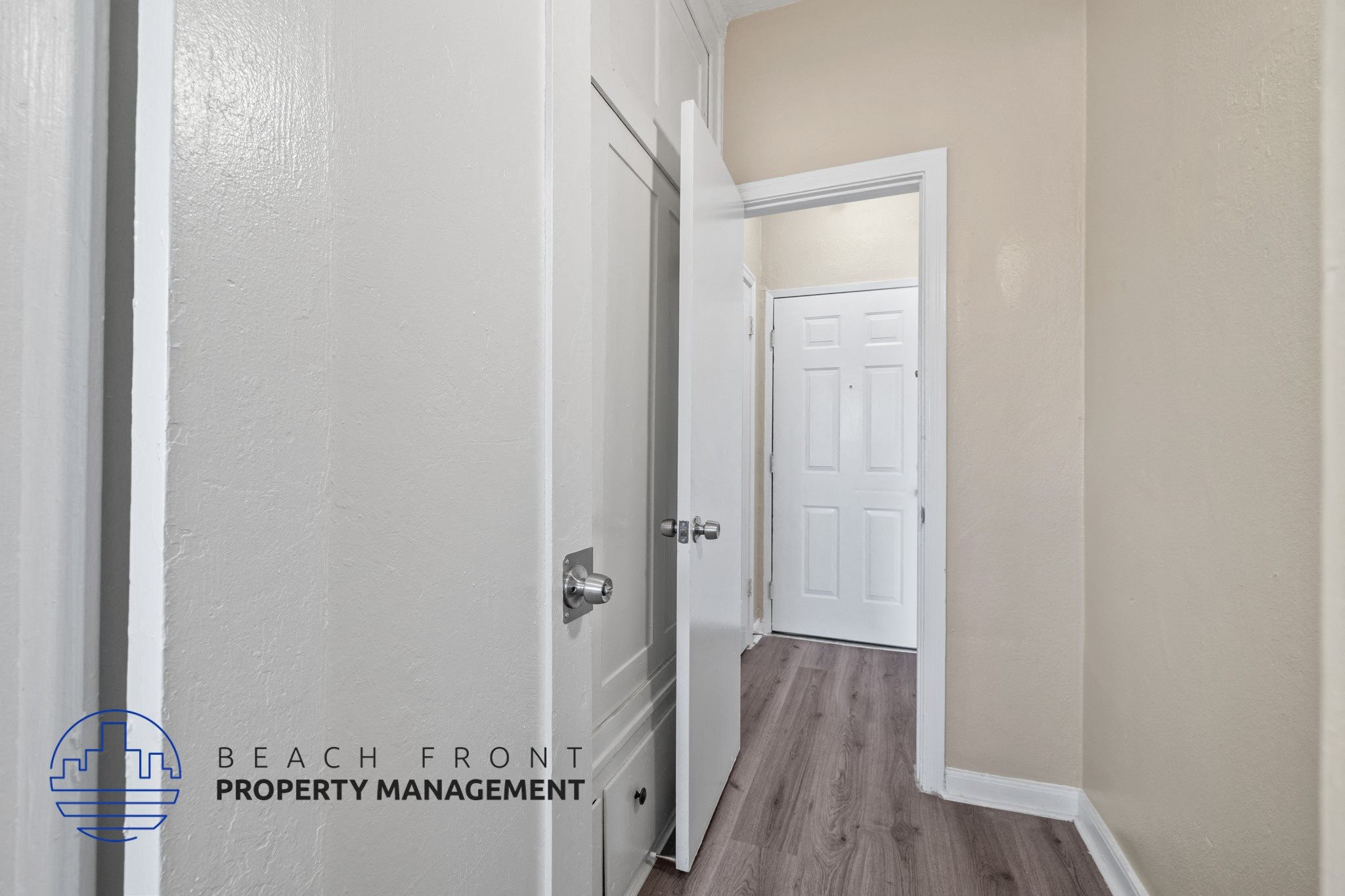A hallway with a white door and a logo for Beach Front Property Management.
