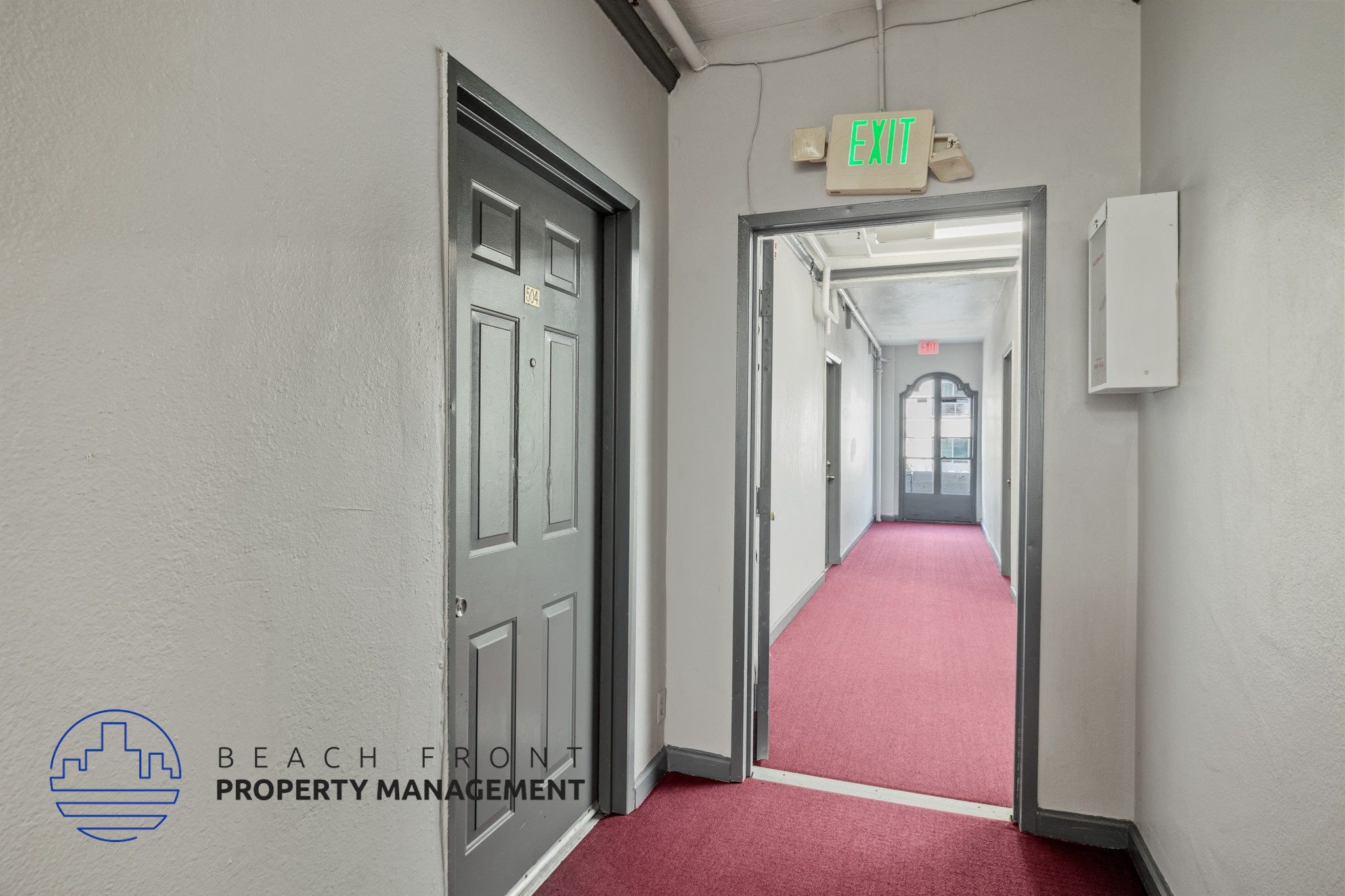 A hallway with a red carpet and a green exit sign.