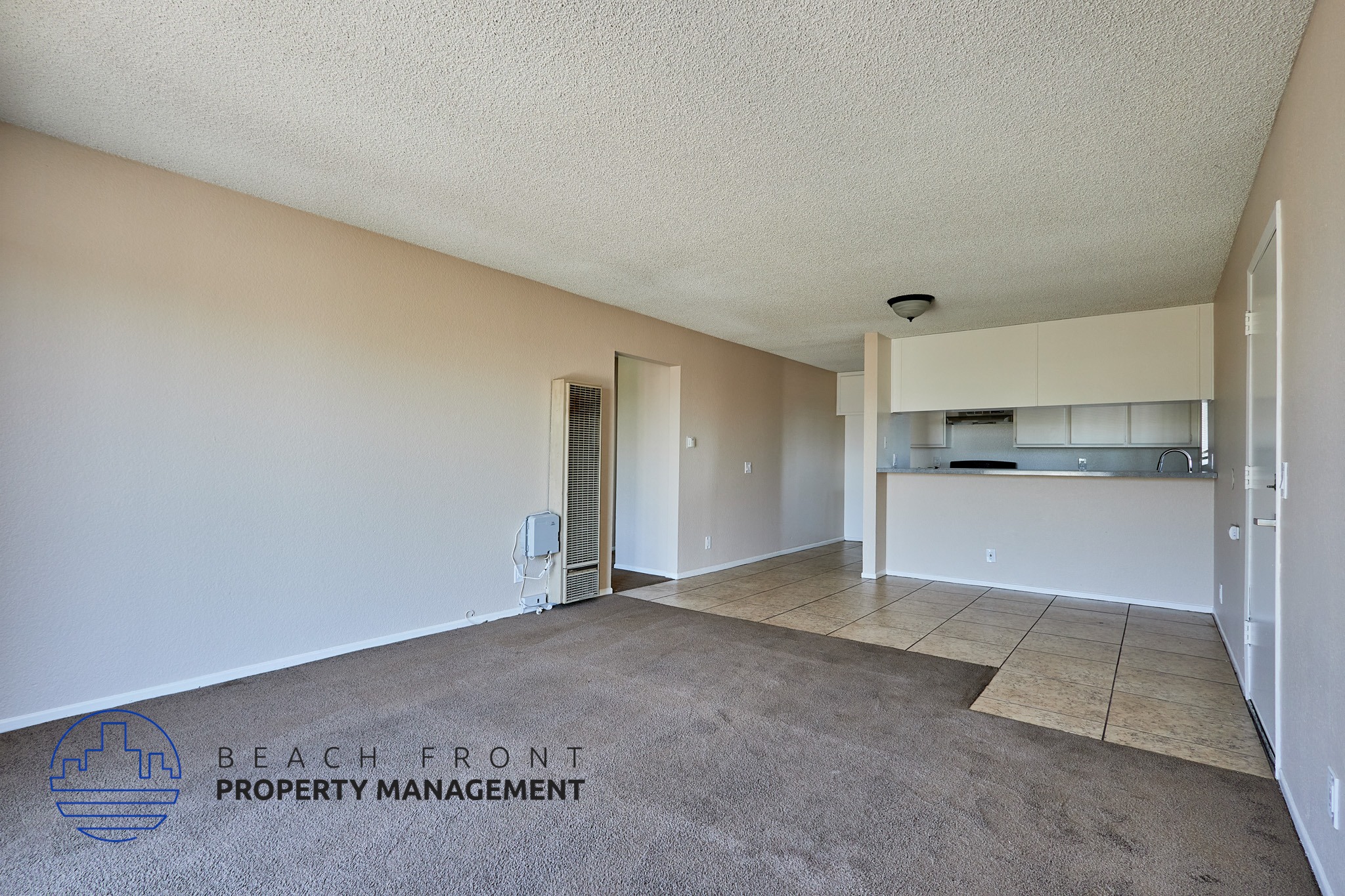 A spacious room with a carpeted floor and a logo for Beach Front Property Management in the corner.