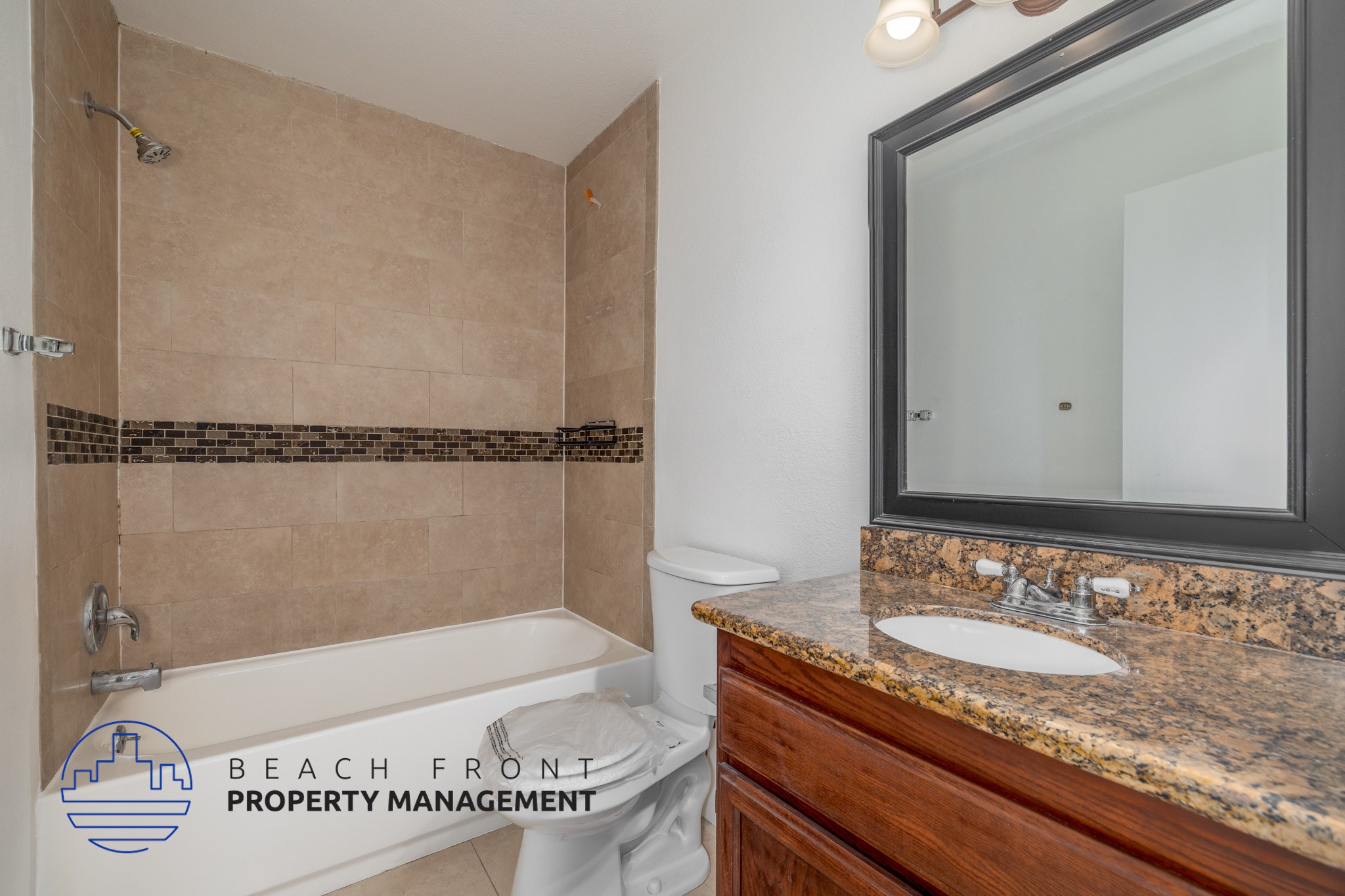 A bathroom with a beige tiled shower, a white toilet, a sink with a granite countertop, and a mirror above the sink.