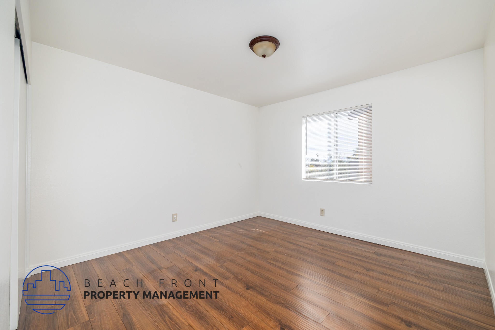 A room with wooden flooring and a window with blinds.