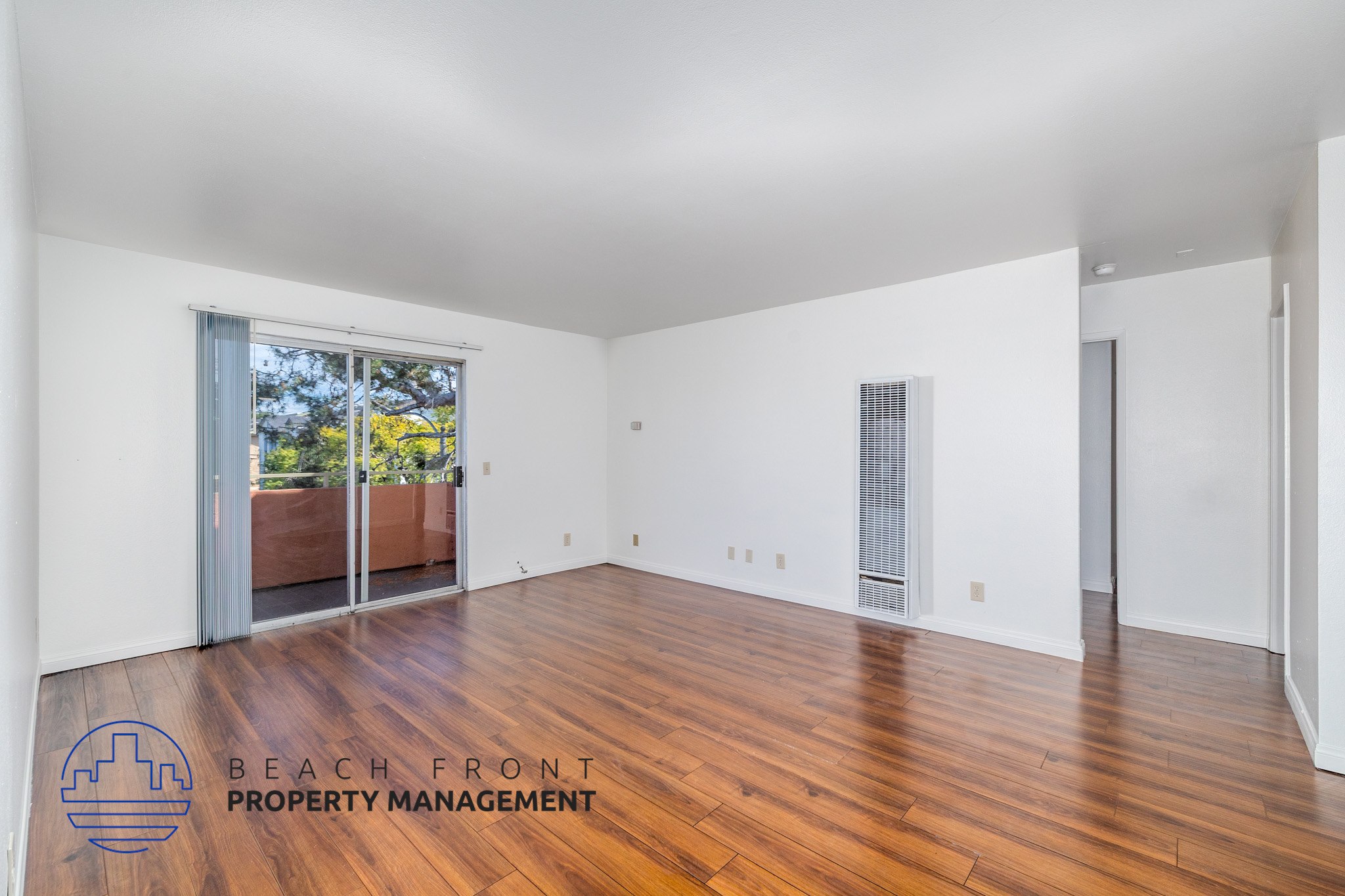 A spacious room with wooden floors and white walls, with a view of a balcony outside.