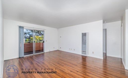 A spacious room with wooden floors and white walls, with a view of a balcony outside.