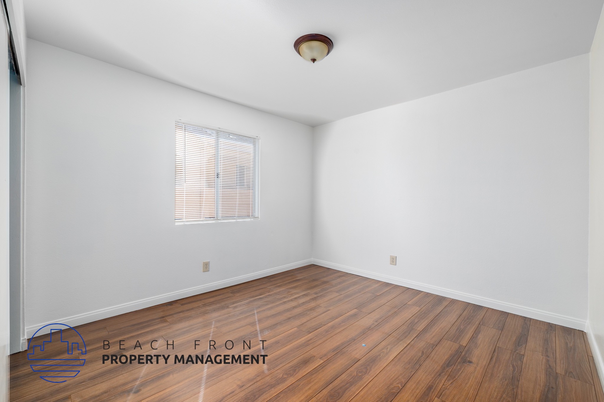 A room with wooden flooring and a window with blinds.
