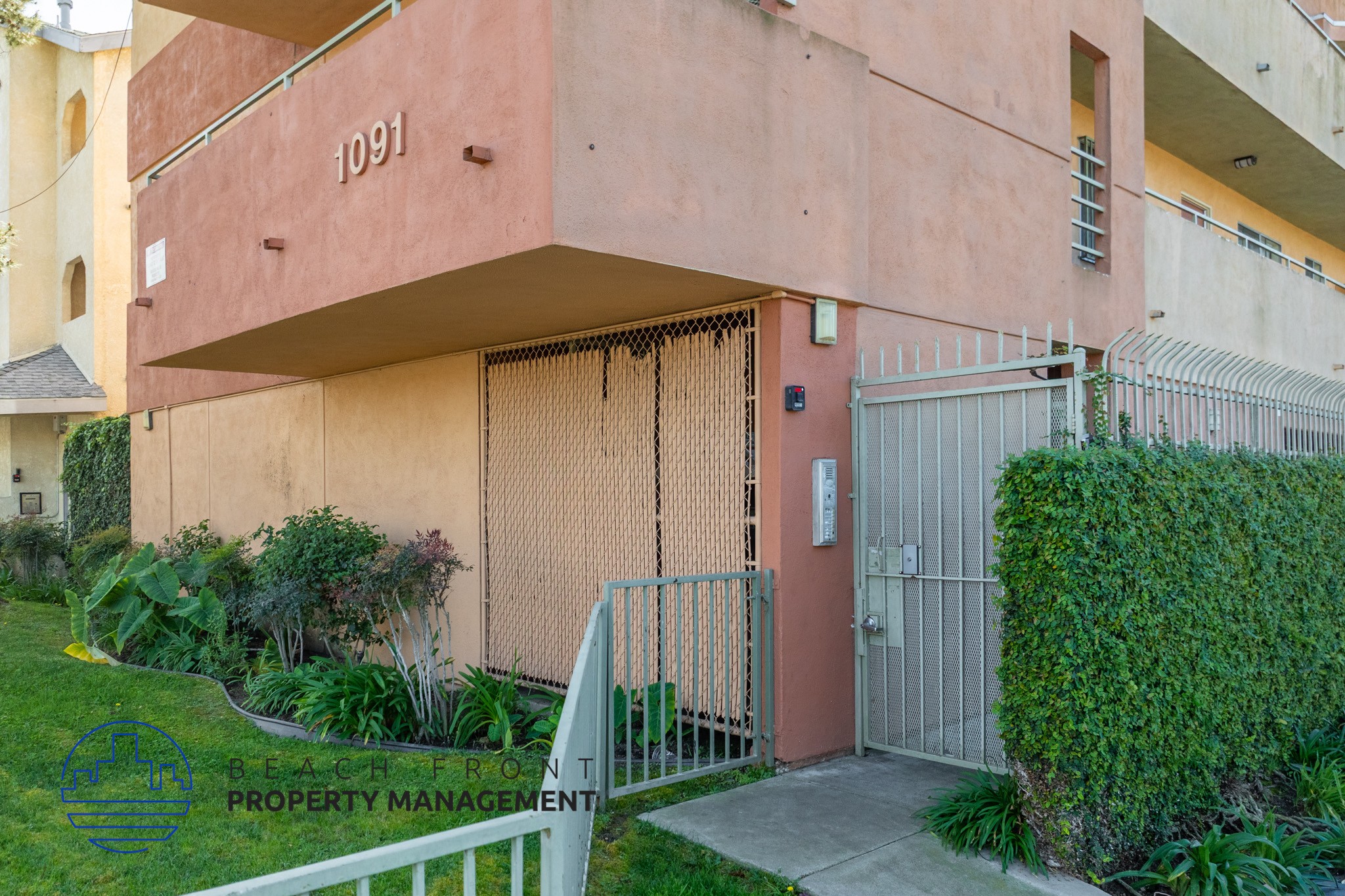 A building with the number 1091 on it is surrounded by a green lawn and a metal gate.