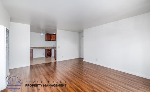 A spacious room with wooden flooring and white walls, with a logo for Beach Front Property Management in the bottom left corner.