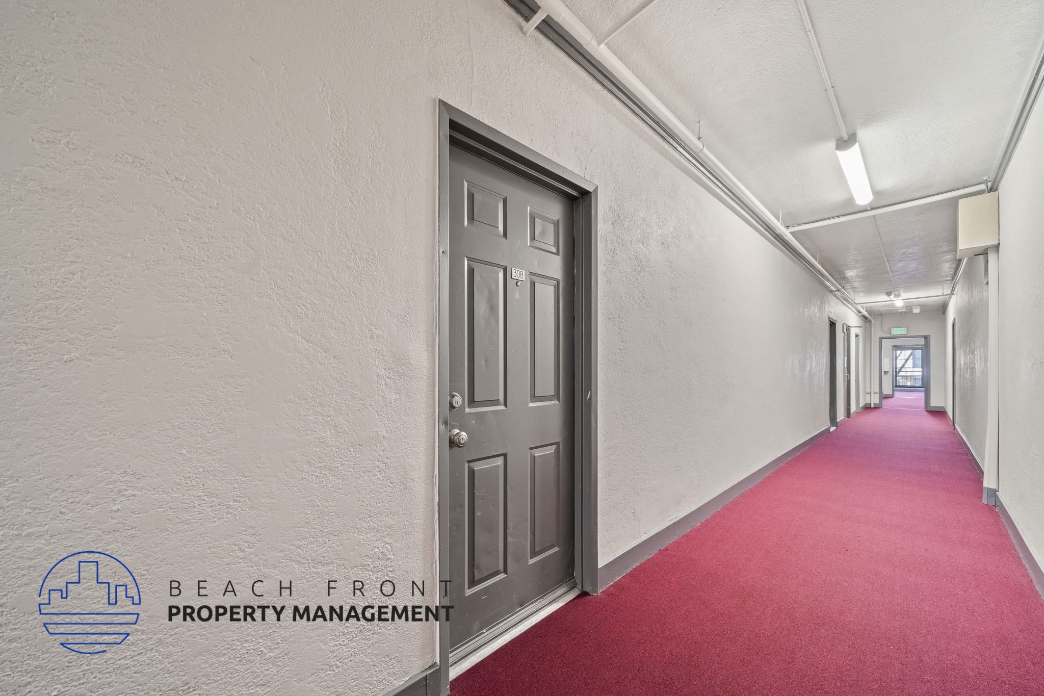 A long hallway with a red carpet and a door on the left side.