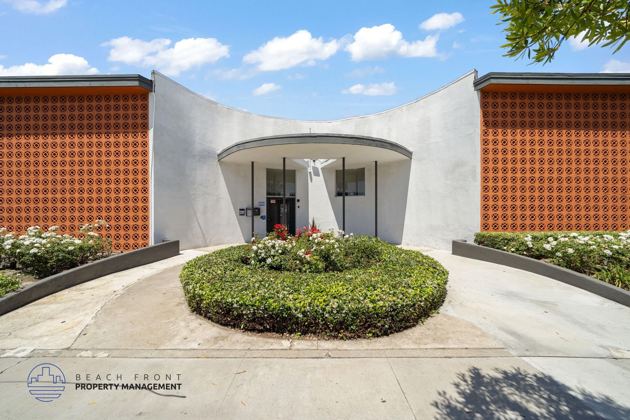A modern building entrance with a circular flower bed in front.